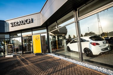 Eingangsbereich des Autohauses Strauch mit großer Glasfront, einem weißen Opel-Fahrzeug im Showroom und einem gelben Willkommen-Schild.