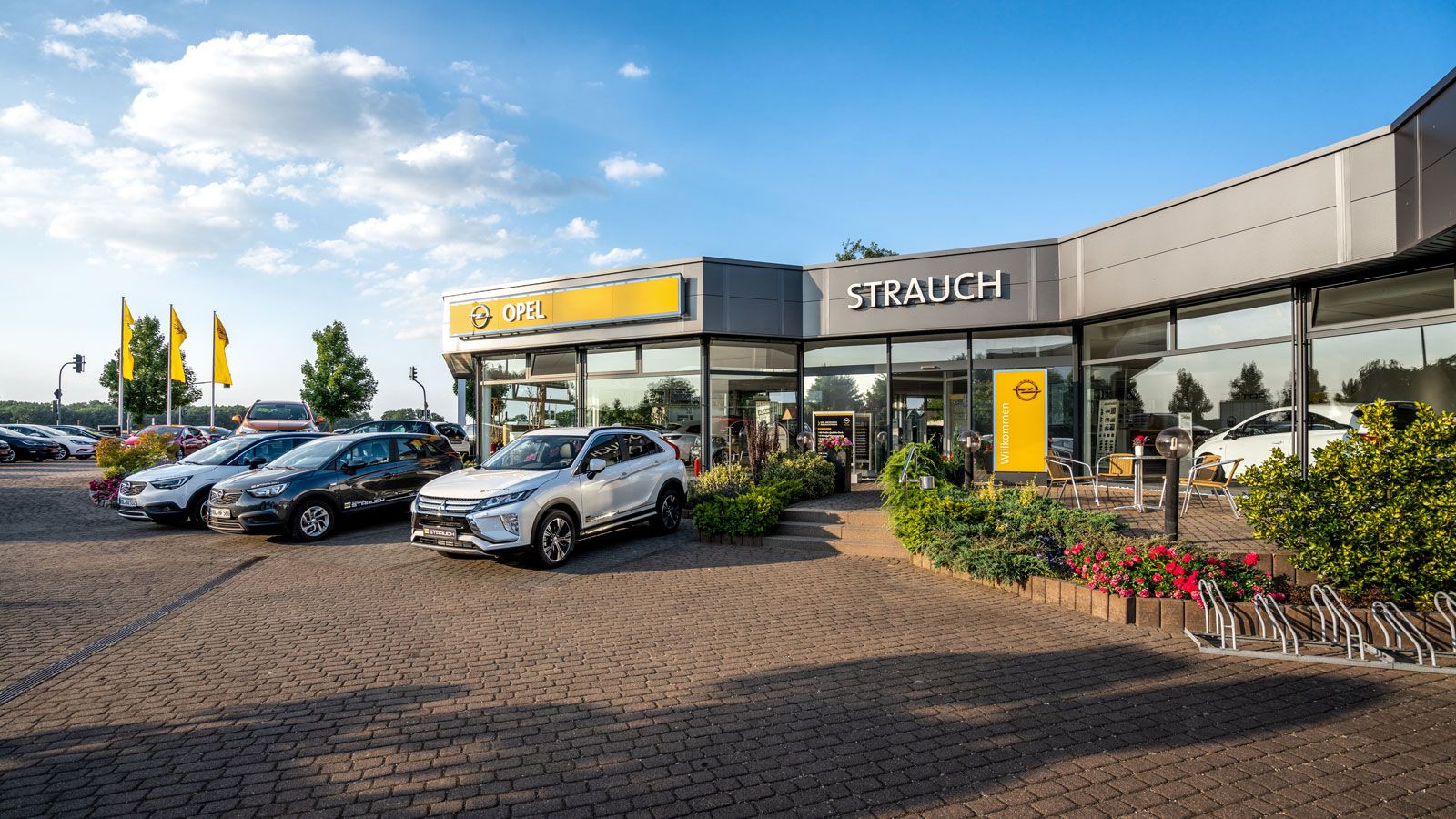 Vorderansicht des Autohauses Strauch in Rüdersdorf mit Opel-Logo, modernen Glasfassaden und einer Auswahl an Fahrzeugen auf dem Außengelände.